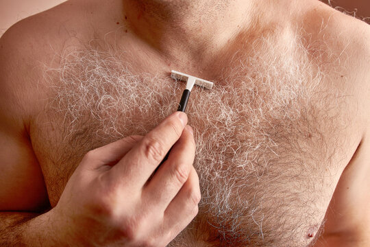 A man shaves his long gray chest hair with a hand razor.