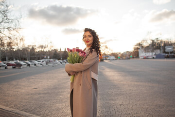 35 years old woman is walking with a bouquet of flowers in the spring streets of the city