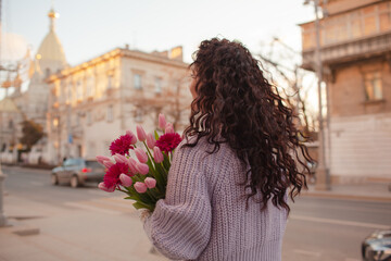 nack view of curly hairs 35 years old woman is walking with a bouquet of flowers in the spring...