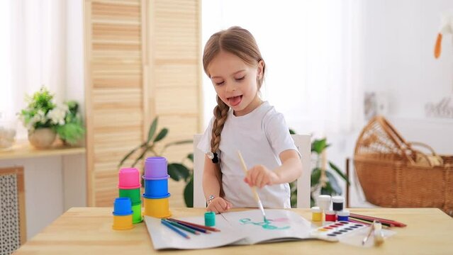 a little girl draws drawings with multicolored paints or learns to draw in a bright children's room at home or in kindergarten, a smiling child, the lifestyle of a preschooler child.