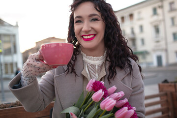 35 years old woman is drinking coffee or tea in cafe with a bouquet of flowers in the spring...