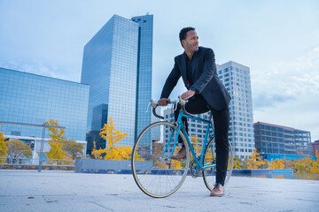 Stylish African American businessman in suit going to the office by bicycle in financial district....