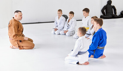 Group of little boys, children in kimono sitting on floor around coach. Children training indoors....