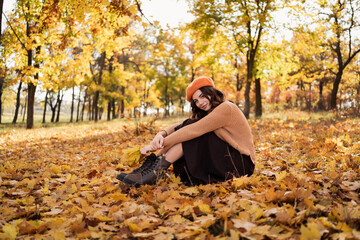 Stylish young woman having rest with leaves in autumn park. Relaxation, enjoying, solitude with nature