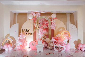 Arch decorated pink balloons, rainbow, text baby one, flowers, paper decor butterfly, and wooden...