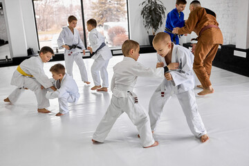 Little boys, children in white kimono training judo, jiu-jitsu sport activity indoors with professional coach. Concept of martial arts, combat sport, sport education, childhood