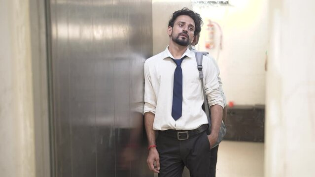 Unhappy tired young boy in formal dress having deep thought exit from lift. Sad Indian bearded man in tie hand in pocket thinking about lost jobless career. Depression, crisis, hopeless unemployment