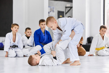 Fototapeta na wymiar Little boys, children in white kimono training judo, jiu-jitsu indoors. Professional sports club for kids. Concept of martial arts, combat sport, sport education, childhood, hobby