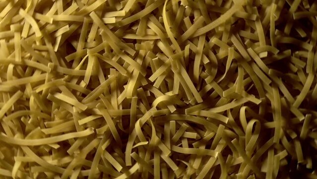 Uncooked Tagliatelle Lungo pasta rotating in fast motion - top view, flat lay, low key, food background. Raw dried organic golden long macaroni texture. Italian food, cuisine and culture close up