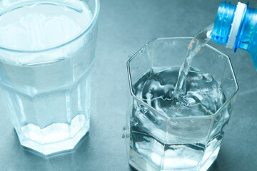 Pouring water from bottle into glass on grey background. Refreshing drink. Healthy lifestyle and...