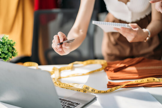 Team female fashion designers design a clothes using a laptop computer with a digital tablet in a modern studio in the morning. - Powered by Adobe