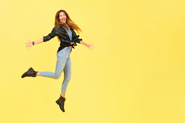 Fototapeta na wymiar Yellow background, a girl in a leather jacket in the style of rock, shows emotions, free space for text, jumps