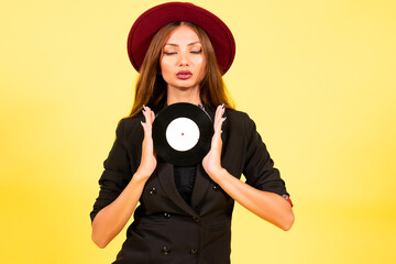 Obraz premium girl in a black suit on a yellow background with a record in her hands, music, the girl shows emotions