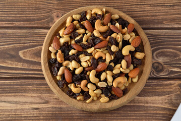Nuts mixture of almond, cashew, peanut and raisin in wooden plate on wooden table