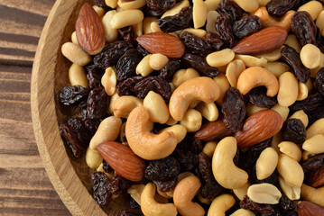 Nuts mixture of almond, cashew, peanut and raisin in wooden plate on wooden table close-up view