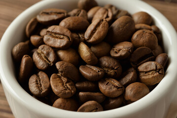 Roasted coffee beans in white cup macro view