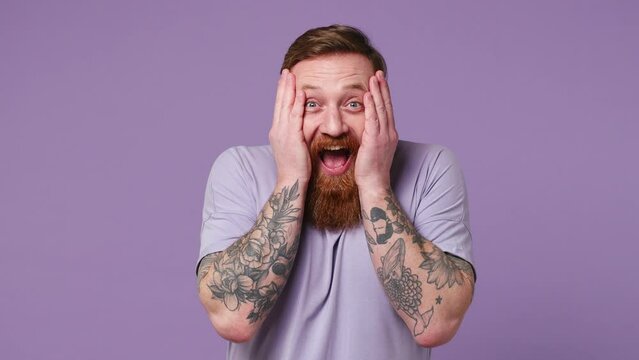 Joyful jubilant surprised fun shocked young man 30s wear casual clothes say wow omg what spreading hands doing winner gesture put arms on face screech isolated on plain pastel light purple background