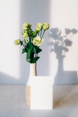 Bouquet of eustoma flowers in vase and blank card on a table in sunlight. Mockup