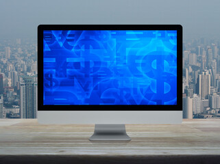 Financial currency symbol on desktop computer monitor screen on wooden table over office building tower and skyscraper in city