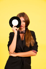 Obraz premium girl in a black suit on a yellow background with a record in her hands, music, the girl shows emotions