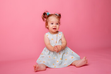 baby girl in a beautiful dress sitting on a pink background