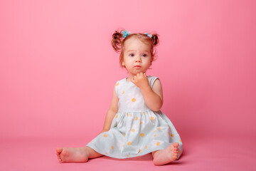 Obraz na płótnie Canvas baby girl in a beautiful dress sitting on a pink background