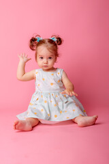 baby girl in a beautiful dress sitting on a pink background