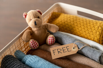 Plastic Box with used clothing and bear toy to donate on wooden table. Reuse. Free label