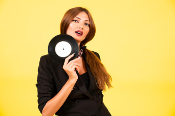 Obraz premium girl in a black suit on a yellow background with a record in her hands, music, the girl shows emotions