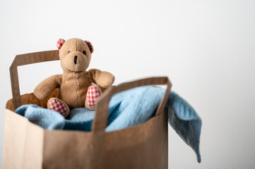 Paper bag with used clothing and bear toy to donate on wooden table. Reuse