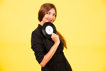 Obraz premium girl in a black suit on a yellow background with a record in her hands, music, the girl shows emotions