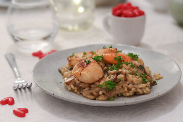 A plate of Italian rice risotto with scallops top with chopped parsley. With fork and mini red heart shape on table with clear glass in background. Valentines lovers ambiance  