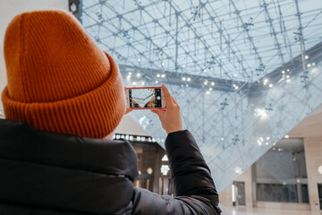 Young woman taking a photo. Inverted pyramid in the shopping mall 'Carrousel du Louvre' with people in Paris, France. Louvre museum hosts one of the biggest art collection in the world.
