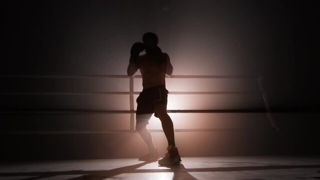 Portrait of unrecognizable man wearing boxing gloves and practicing a knock. Close-up shot of male boxer boosting whole-body strength with a spotlight in the background. High quality 4k footage