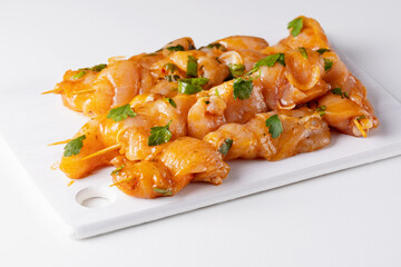 Raw chicken skewers in marinade with spices on a white board. Raw marinated and spicy chicken...
