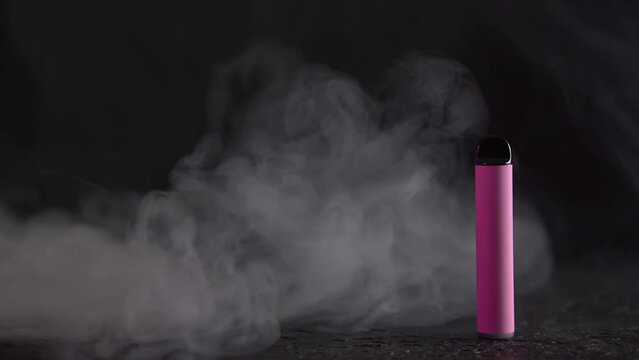 Pink electronic cigarette vape on dark background with smoke. High quality photo