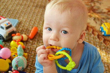 A little boy plays at home with toys. Pulls teether into the mouth