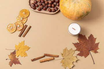 Autumn frame. Space for text. Pumpkin, candle, dried oranges, hazelnuts and maple leaves