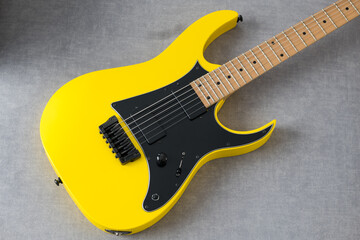 Obraz premium Vibrant Yellow Electric Guitar with Sleek Design and Shiny Surface Standing on a Minimalistic Grey Background in a Striking Stock Photo