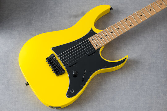 Vibrant Yellow Electric Guitar with Sleek Design and Shiny Surface Standing on a Minimalistic Grey Background in a Striking Stock Photo