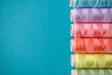 Pastel colors sewing threads on a blue background, multicolored spools, copy space for design