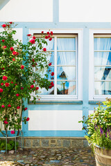 Fototapeta na wymiar Traditional German architecture, facade of old house, windows, blue sky, flowers, paving slab.