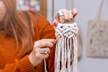Woman craftsman weaves macrame from light cotton threads. Women's hands knit a lace ornament