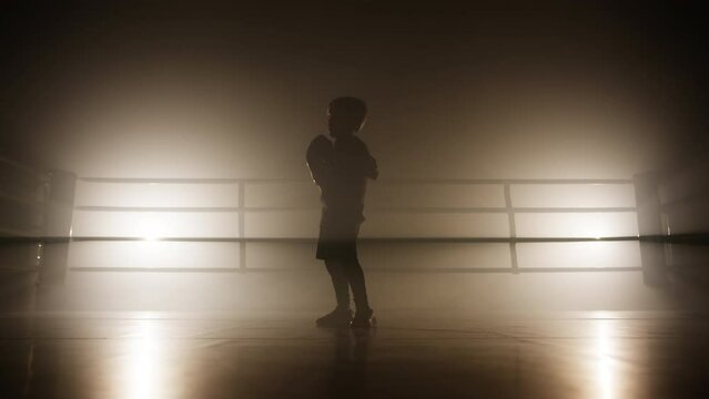 Physical training of young, active boy in boxing ring improving his punches and hitting. Close-up view of a child's silhouette working out alone. High quality 4k footage