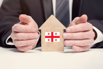 Businessman hand holding wooden home model with Georgian flag. insurance and property concepts