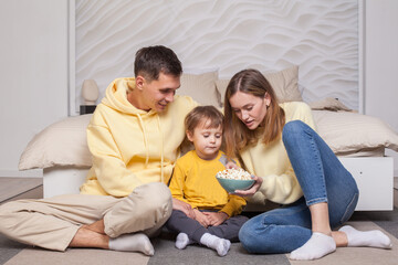 Friendly family, lovely parents with child son sitting by the bed and holding bowl with popcorn