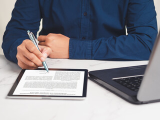 Businessman signing a digital contract or agreement on a tablet while sitting at the table in the...