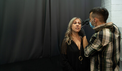 Beautiful older woman in a piercing studio preparing to get a piercing. Young worker marks the area with tweezers. Youthful spirit concept. Copy space on the left