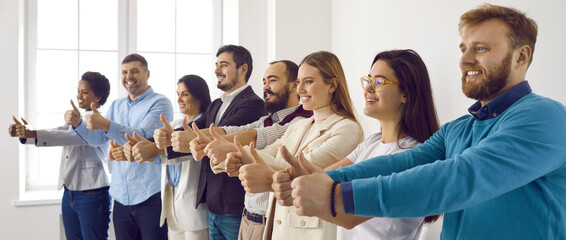 Multiracial group of happy business people showing thumbs up all together. Cheerful male and female employees standing in office, giving thumbs up and smiling. Dream team, teamwork, success concept