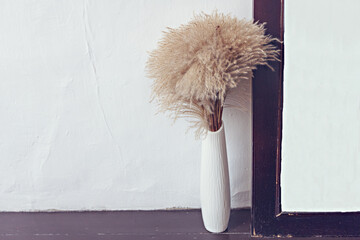White vase with dry grass next to the photo frame and white wall home design minimalism